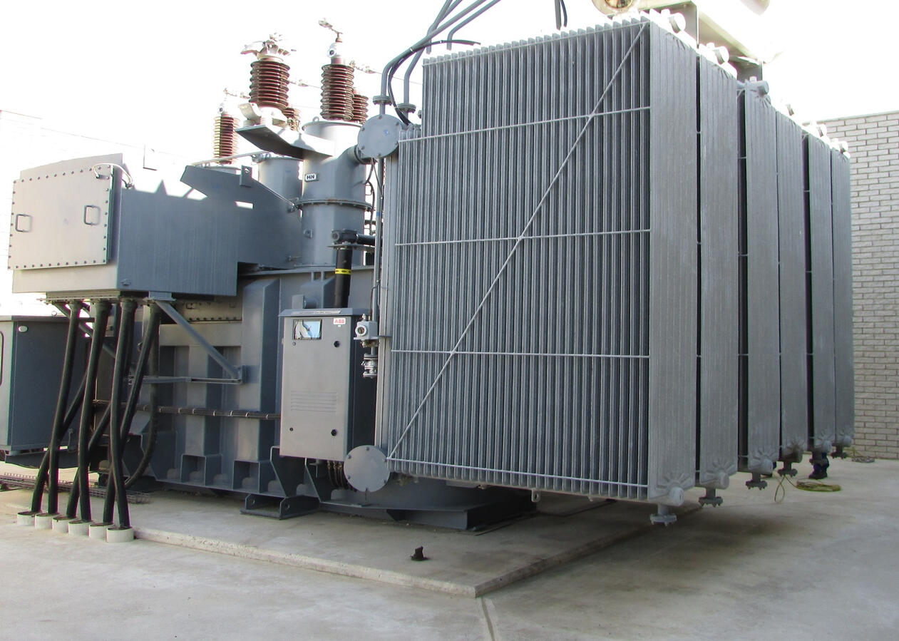 Grey power transformer with cooling fins and electrical bushings.