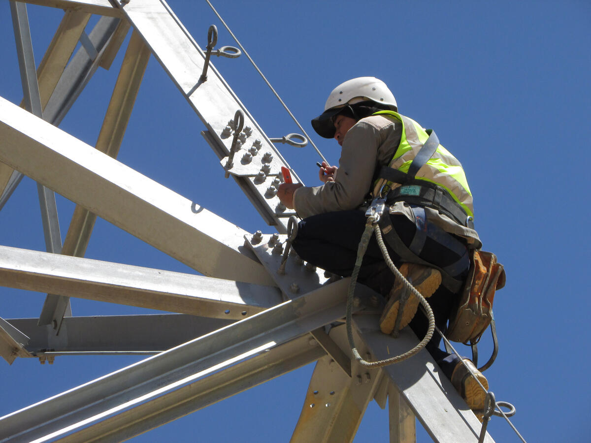 Technician wearing a safety harness working on a steel transmission tower.